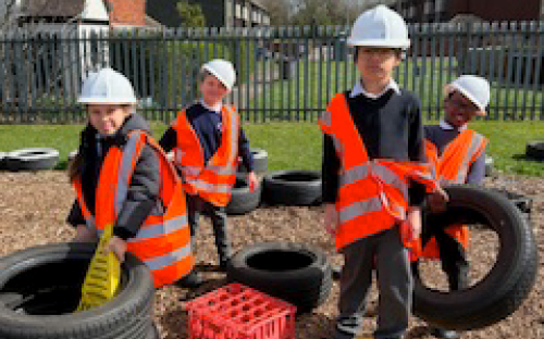 Children in Hi-Vis and hard hats are standing on a building site 